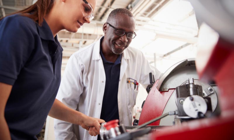 A tutor overseeing a student using engineering machinery